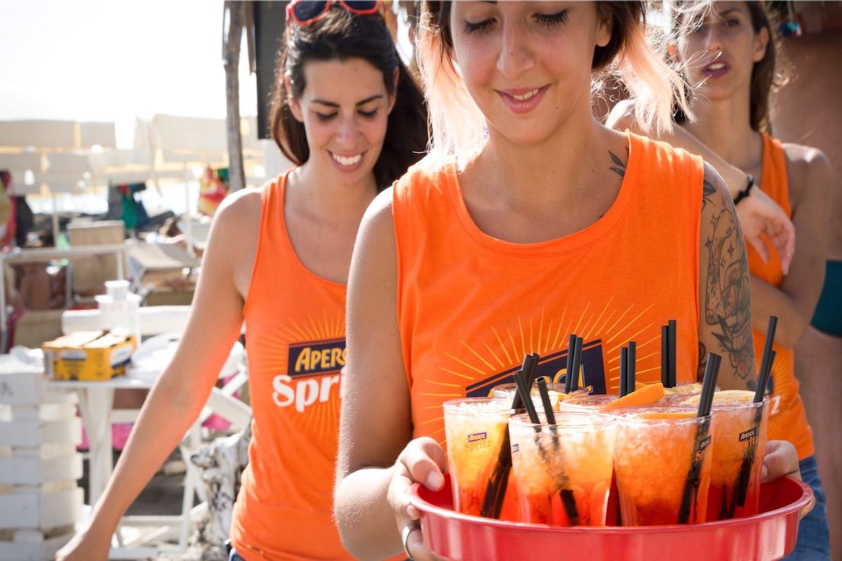 esempio di promozione per attirare i clienti: hostess e promoter per aperol spritz durante assaggio gratuito della bevanda. 